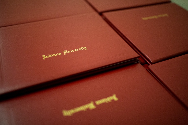 Indiana University diplomas in red folios stacked on a table